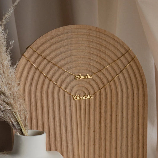 Gold name necklace on a wooden stand with a neutral background