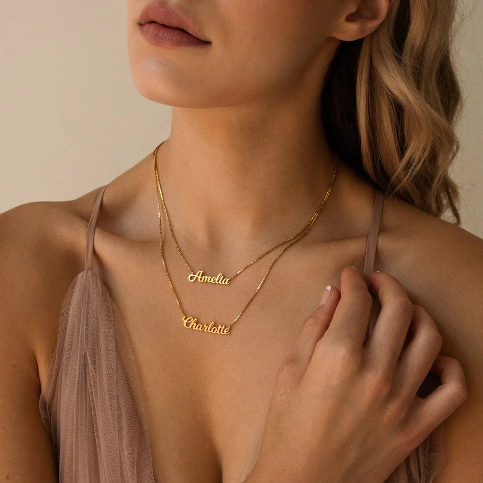 Woman wearing a gold necklace with engraved names against a neutral background