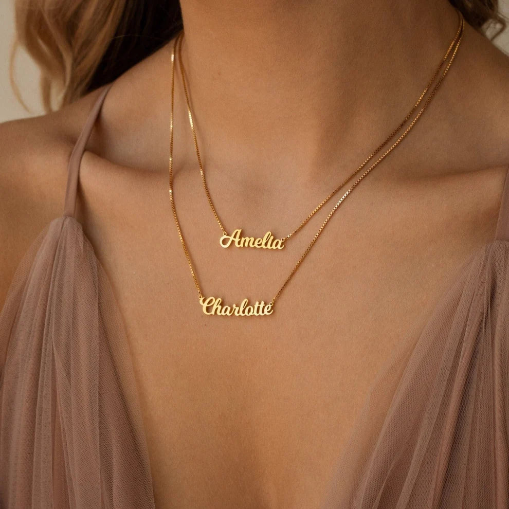 Gold name necklace with 'Amelia' and 'Charlotte' on a person wearing a sheer top.