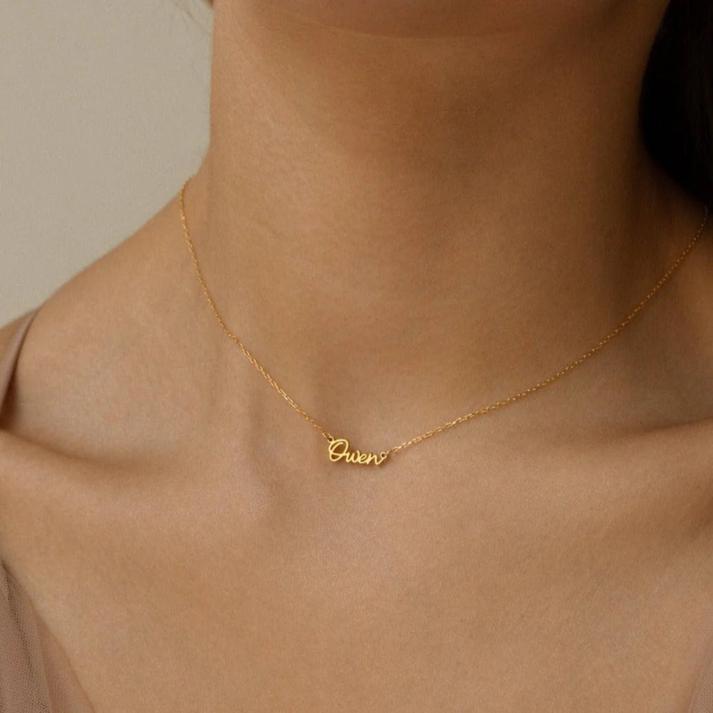 Gold necklace with 'Queen' pendant on a person's neck against a neutral background