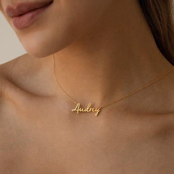 Gold necklace with 'Audrey' pendant on a person's neck against a neutral background