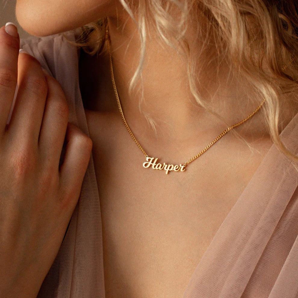 Gold necklace with 'Harper' pendant on a person wearing a sheer pink top.