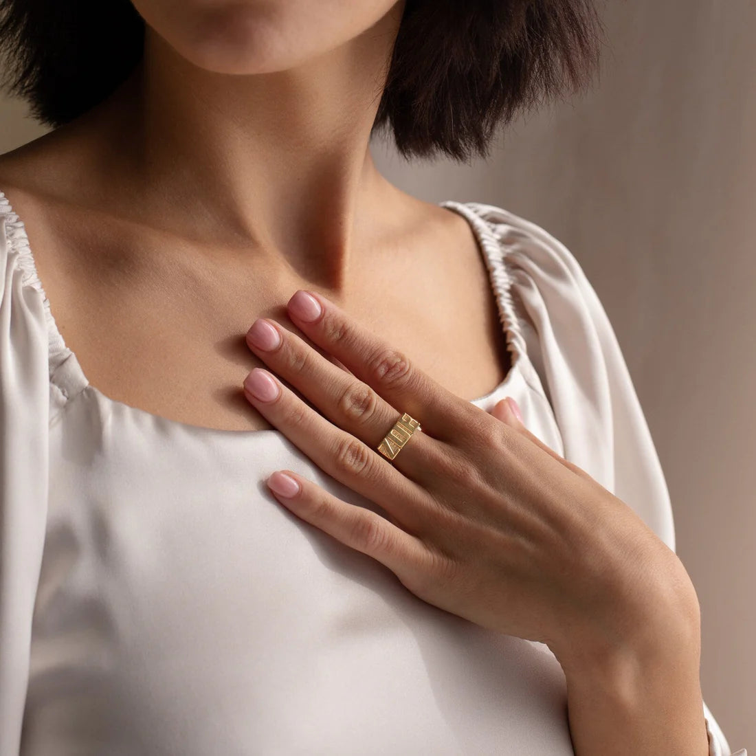 Woman wearing a gold ring on her finger, with a neutral background