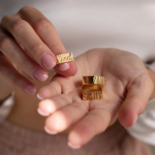 Gold rings with engraved text held in hands against a neutral background