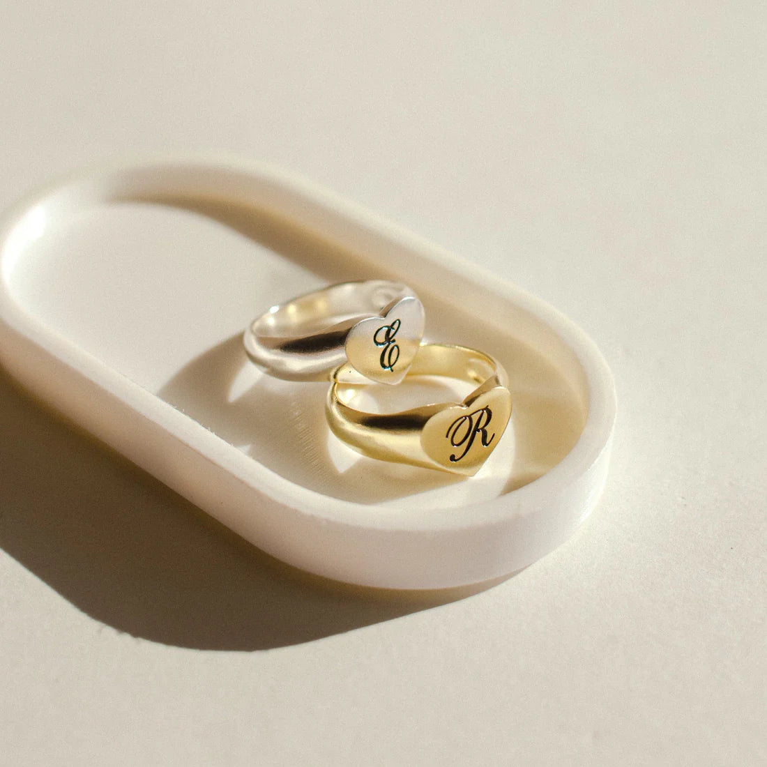 Two gold rings with engraved letters on a white dish