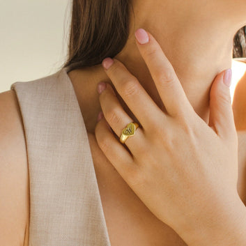 Close-up of a hand wearing a gold ring with a visible brand logo, touching the neck.