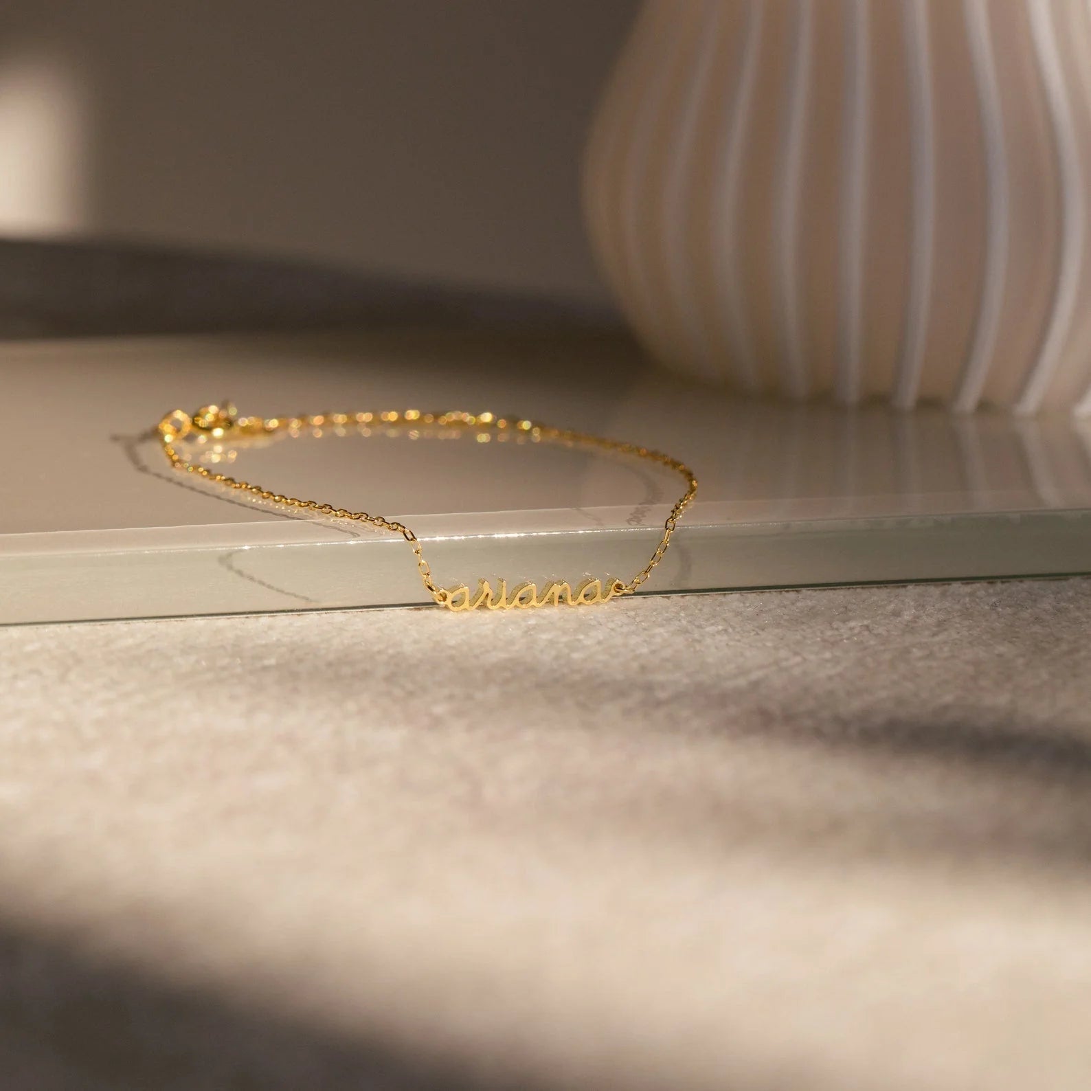 Gold bracelet on a light surface with a blurred vase in the background