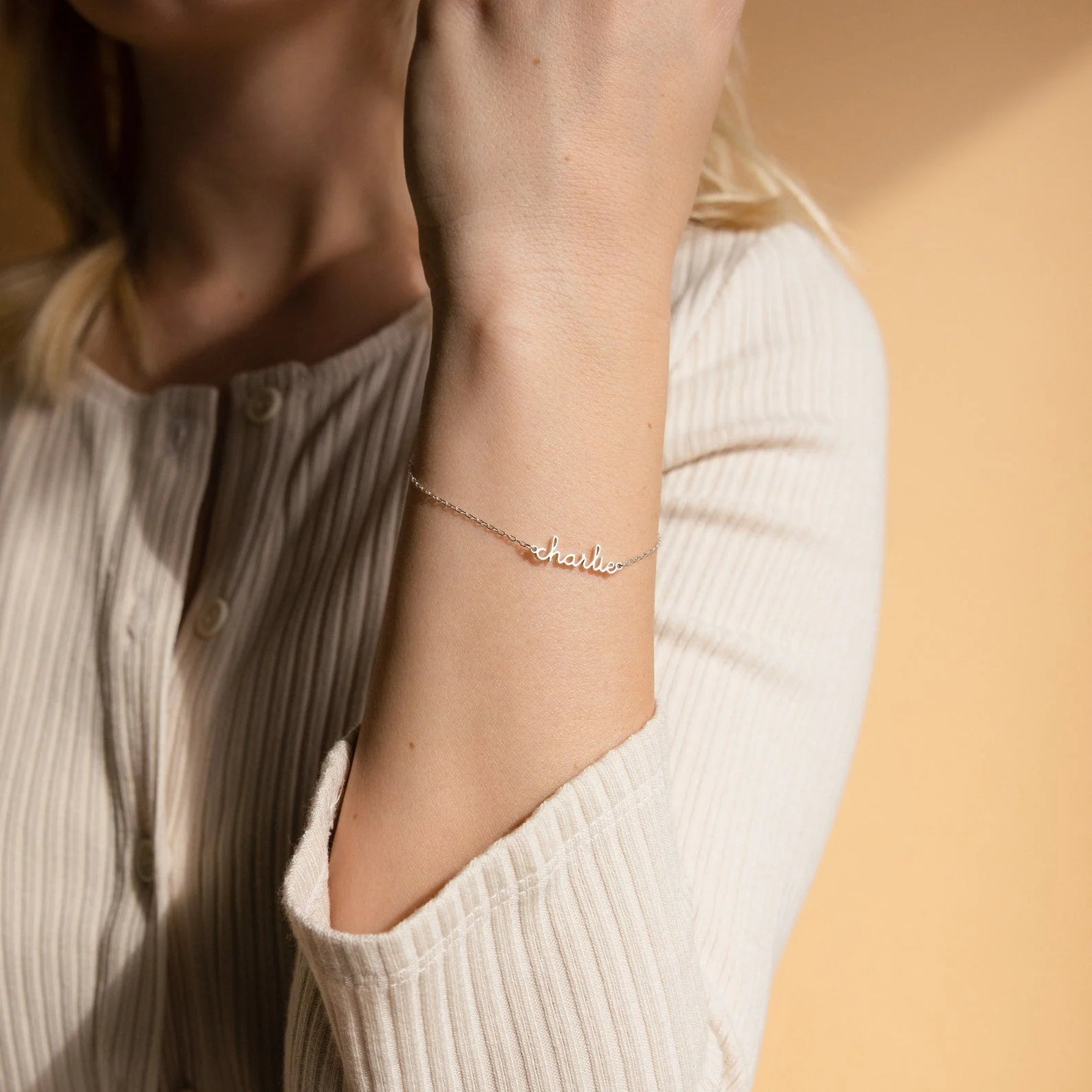 Person wearing a delicate gold bracelet with 'charlie' on it against a neutral background