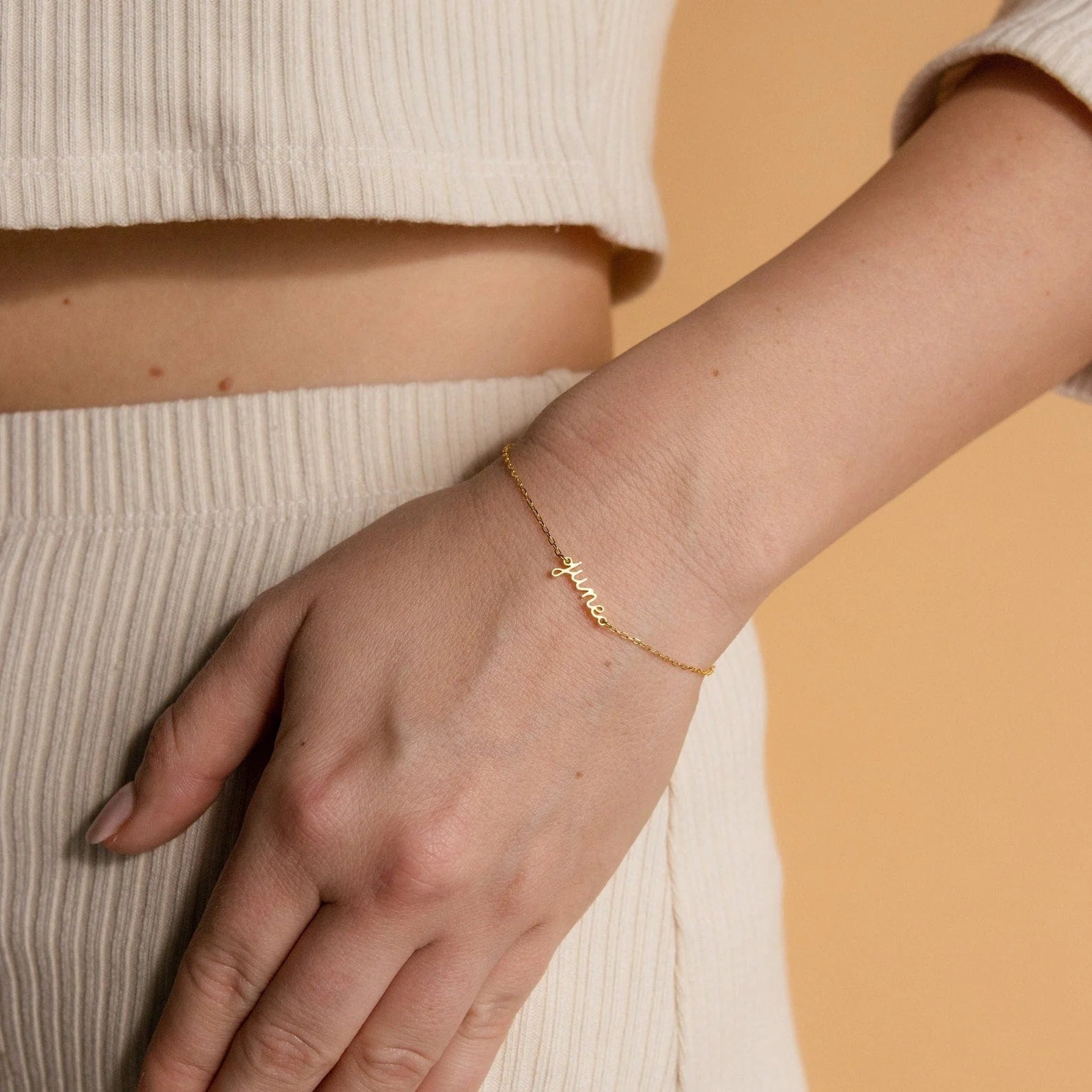 Gold bracelet on a person's wrist against a beige background