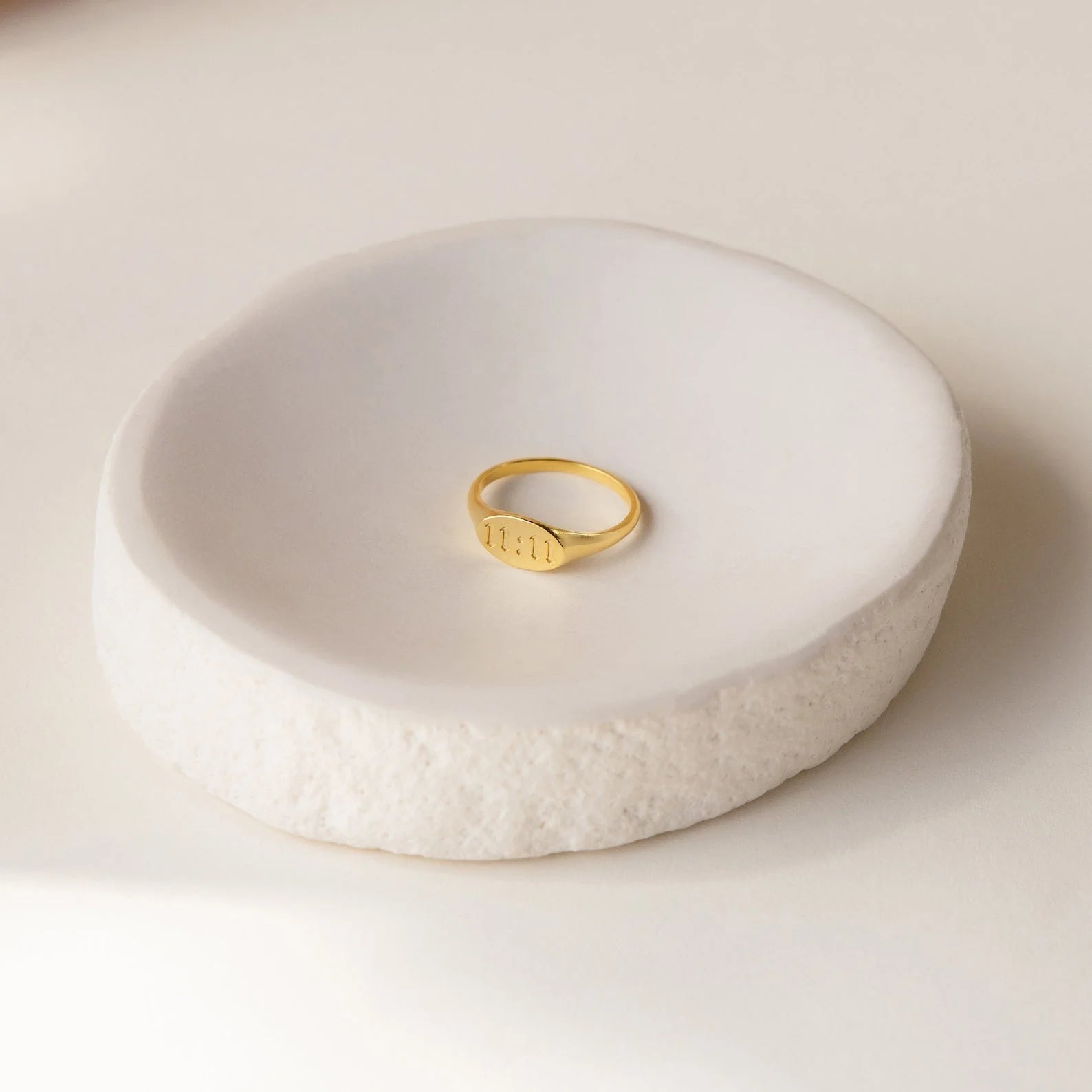 Gold ring on a textured white ceramic dish against a light background