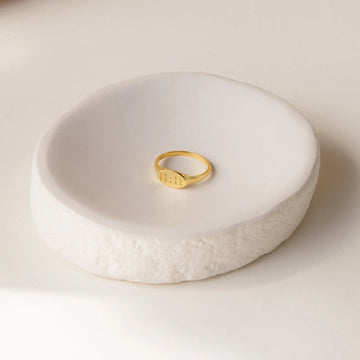 Gold ring on a textured white ceramic dish against a light background