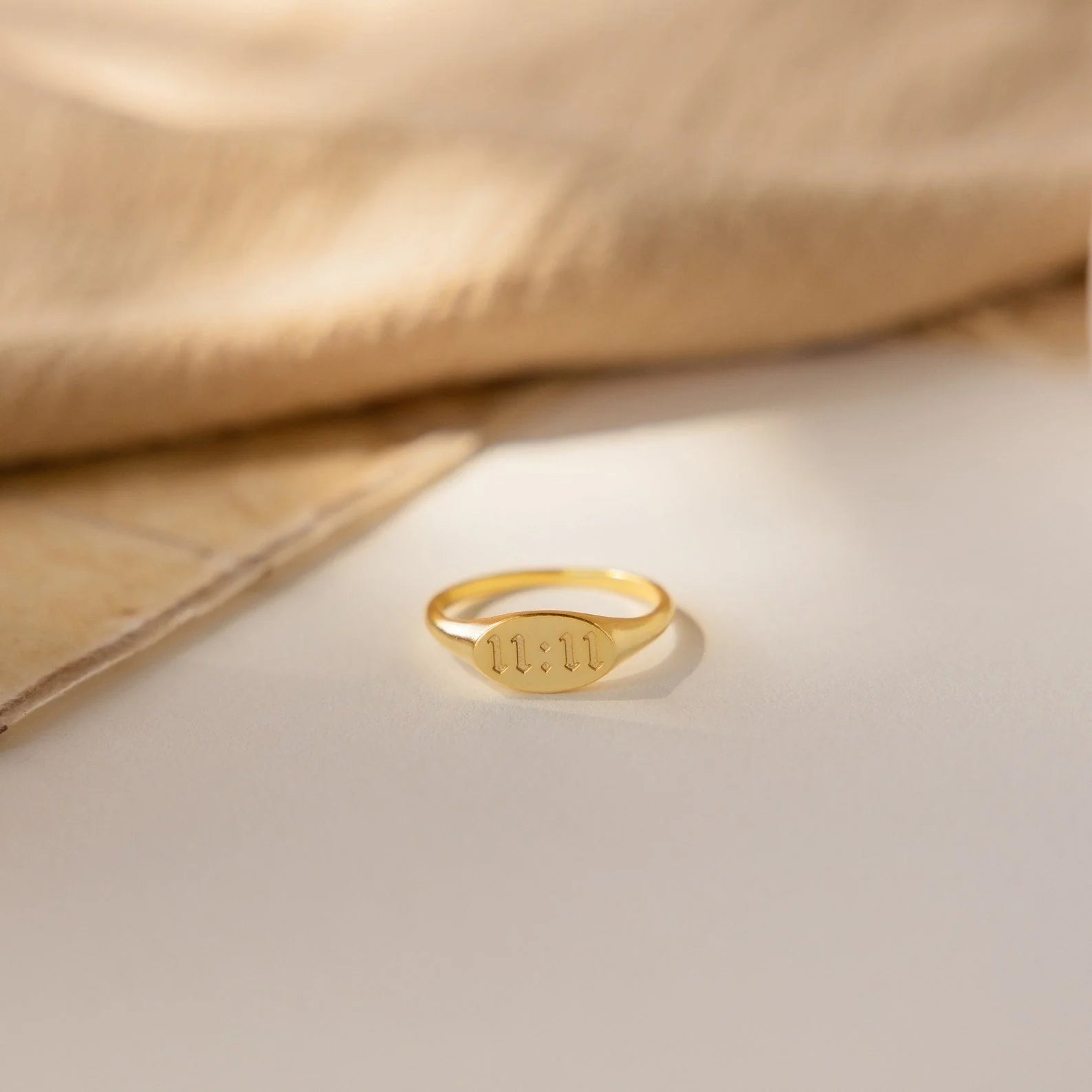 Gold ring with engraved letters on a beige fabric background