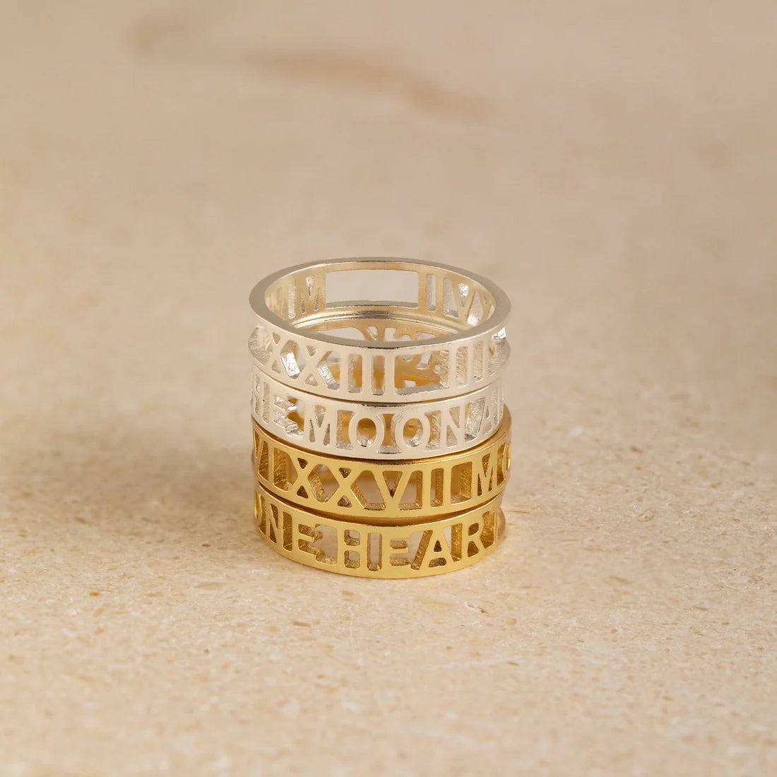 Stack of gold and silver rings with cut-out designs on a beige background