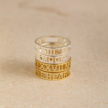 Stack of gold and silver rings with cut-out designs on a beige background