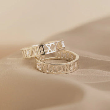 Two gold rings with engraved text on a beige background