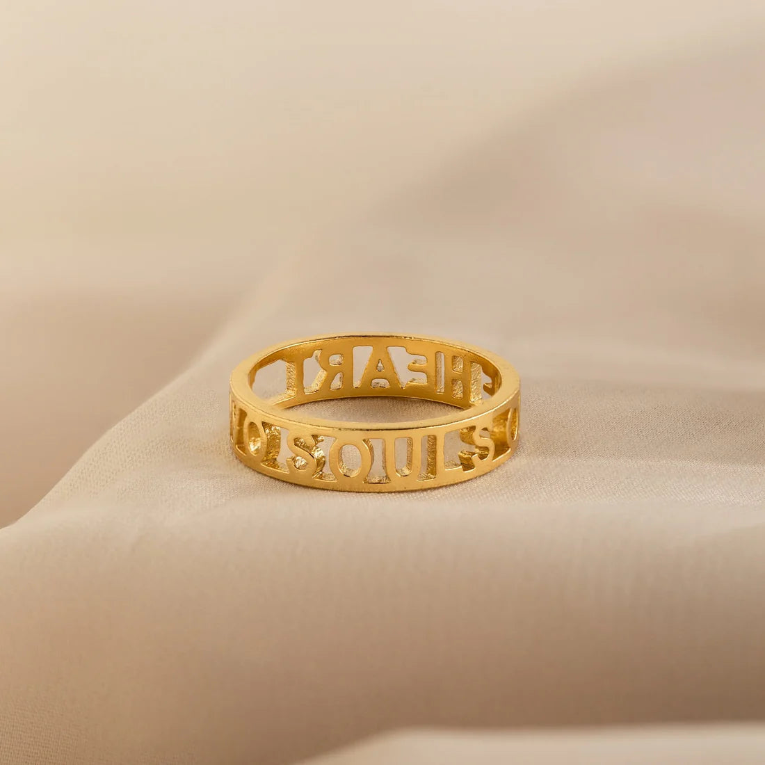 Gold ring with cut-out letters on a beige background