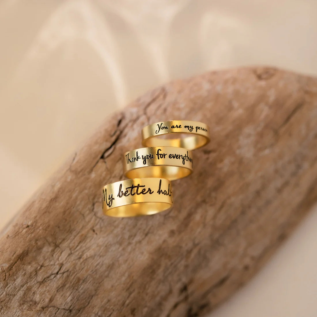 Three gold rings with engraved text on a wooden surface