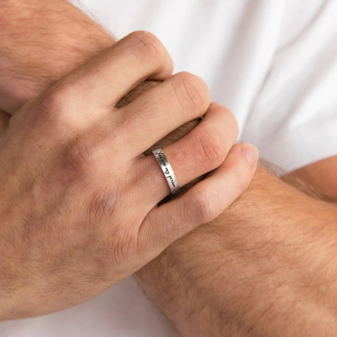 Close-up of a hand wearing a silver ring with engraved text on a white background