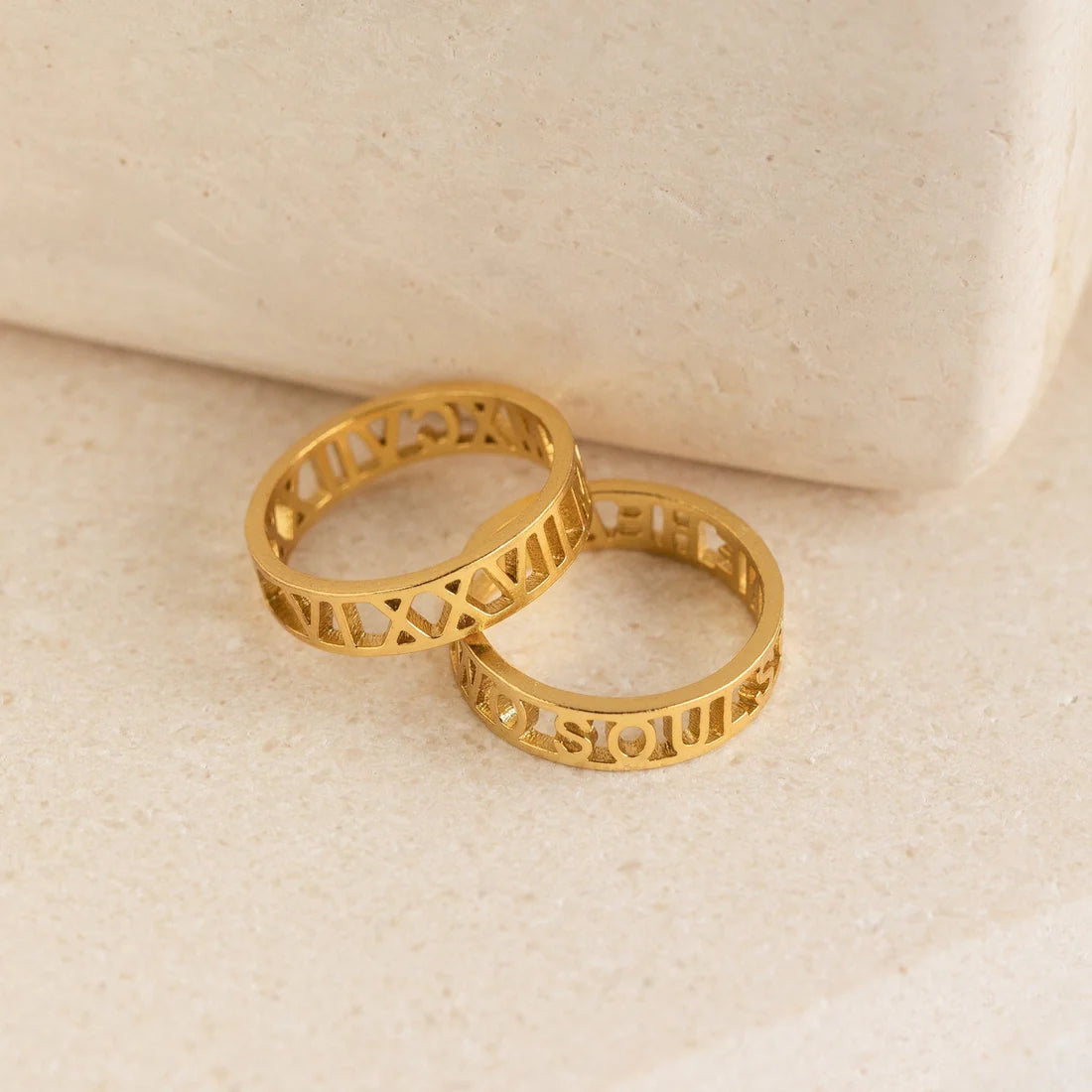 Two gold rings with intricate designs on a beige surface