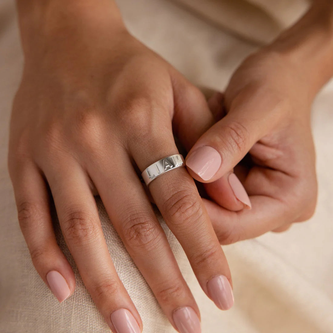 Close-up of two hands with a silver ring on a beige background