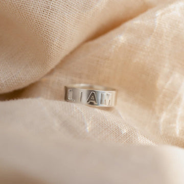 Silver ring with engraved text on a beige fabric background
