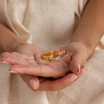 Two gold rings held in a person's hands against a beige background