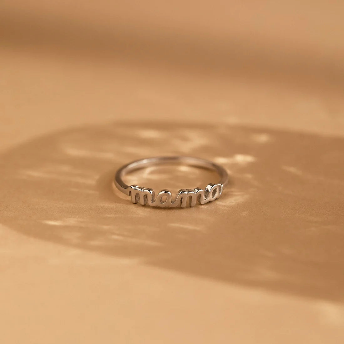 Silver ring with 'mama' engraving on a beige background