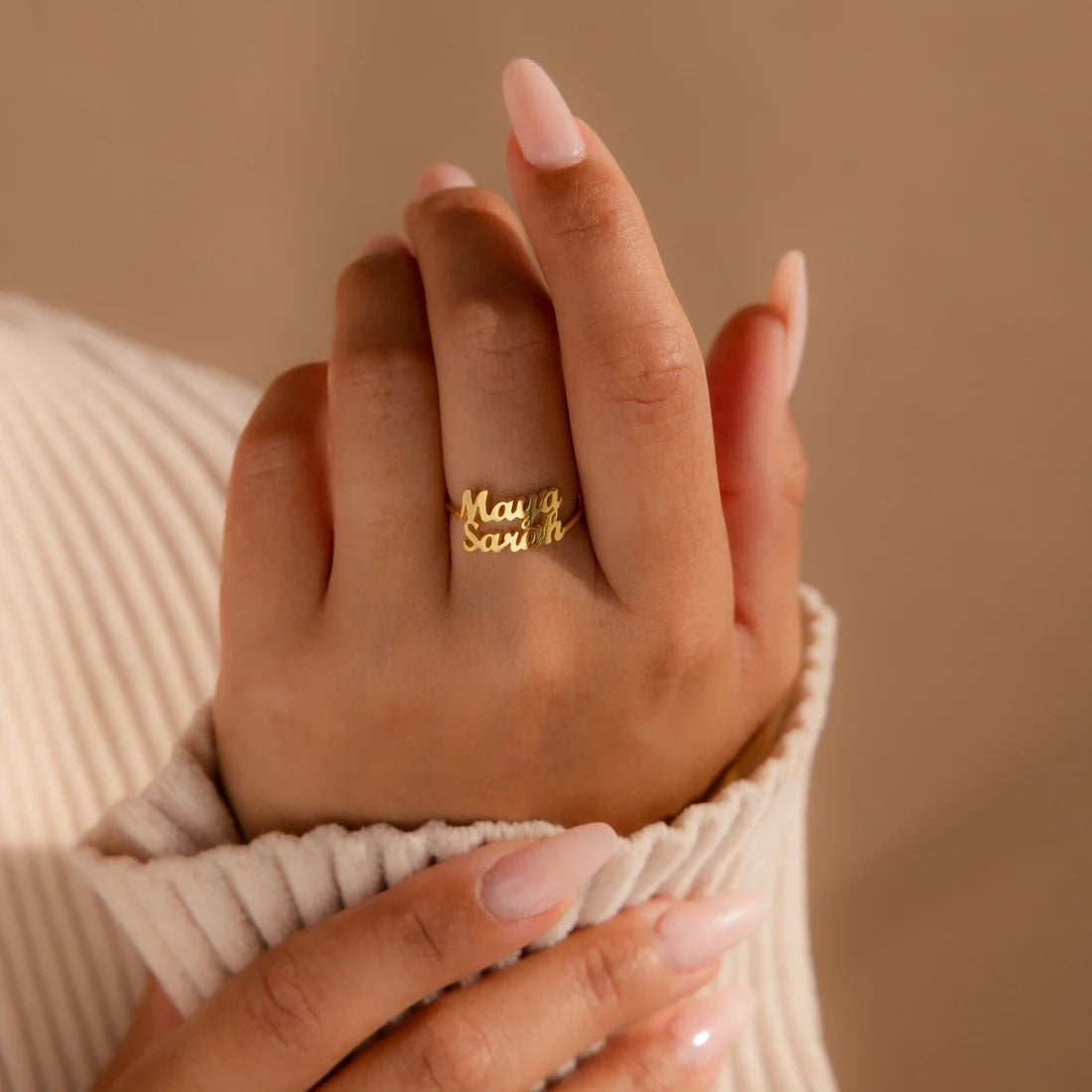 Hand wearing a gold ring with 'Maya' and 'Earth' on a beige background