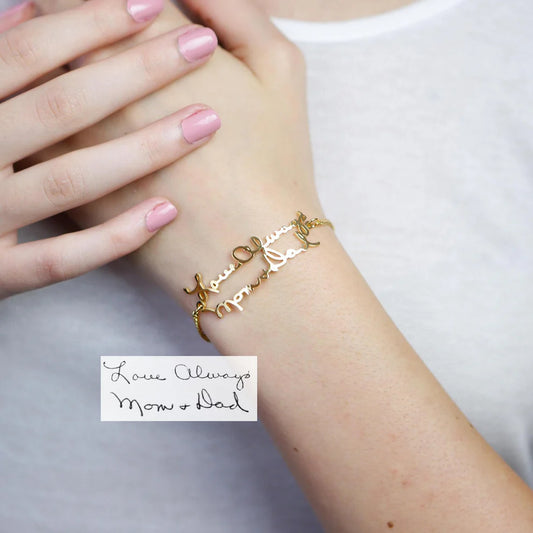 Gold bracelet with engraved text on a wrist, with a card below reading 'Love Always Mom & Dad'.