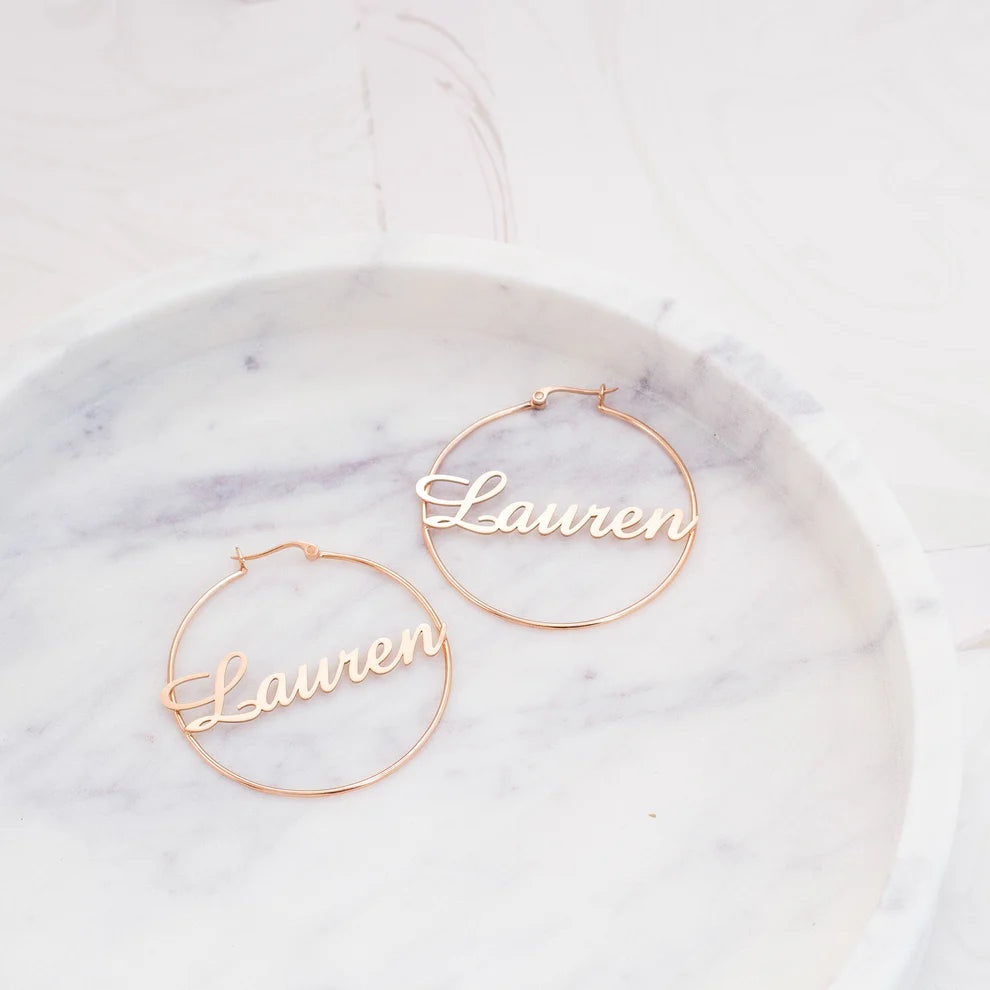 Gold hoop earrings with 'Lauren' engraved on a marble surface