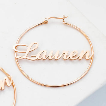 Rose gold hoop earrings with 'Lauren' engraving on a light background
