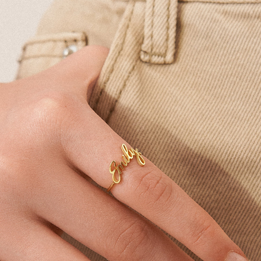 Gold ring with 'girl' on a person's finger against a beige background
