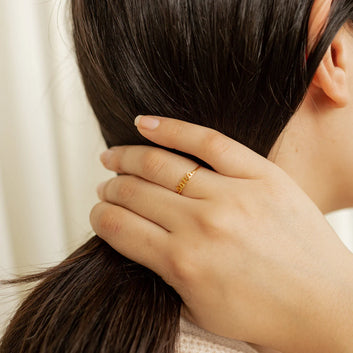 Close-up of a hand with a gold ring gently touching hair, on a neutral background
