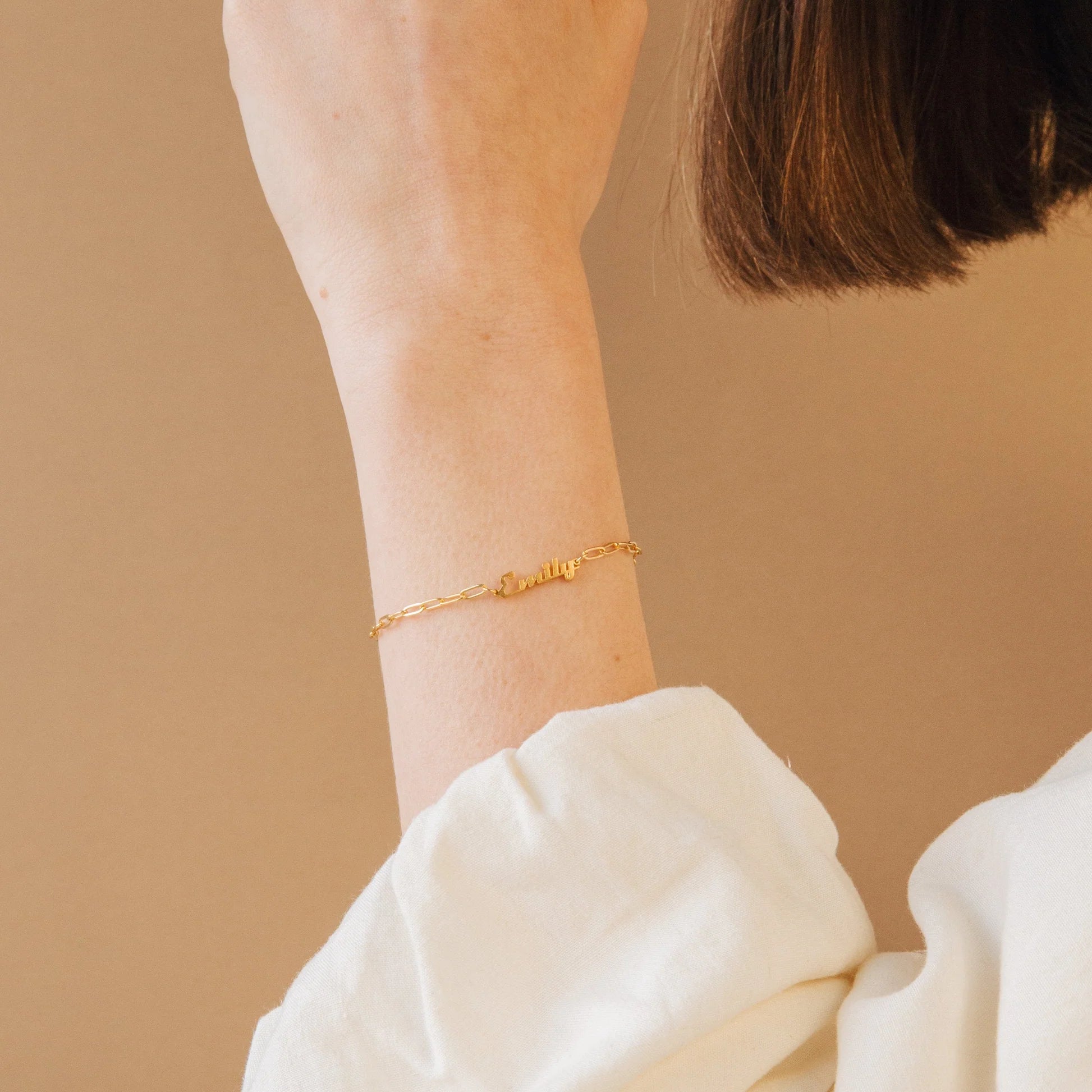 Gold bracelet on a person's wrist against a beige background