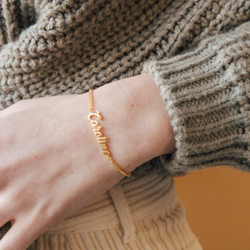 Gold name bracelet on a wrist with a textured sweater sleeve