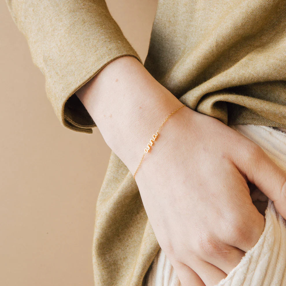Close-up of a hand wearing a gold bracelet with a beige background