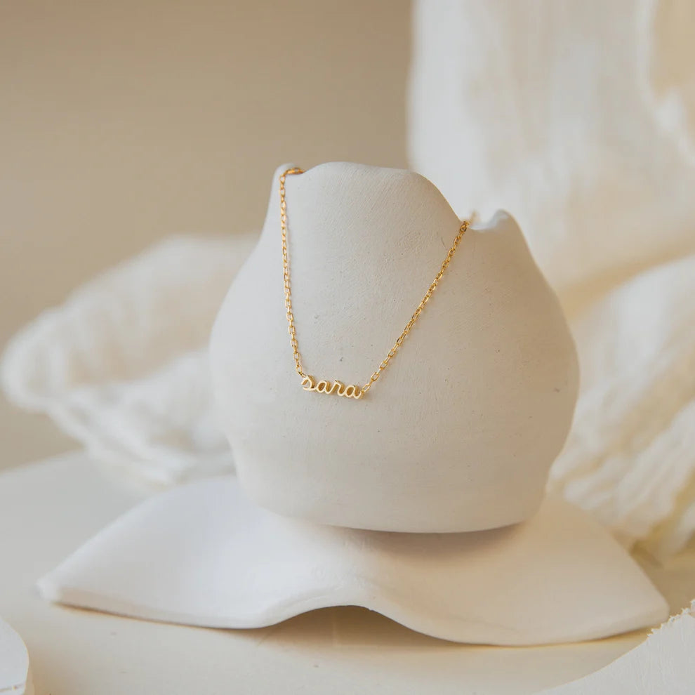Gold necklace on a white ceramic stand with a soft, blurred background