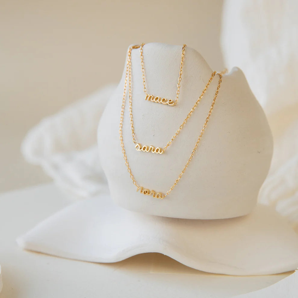 Two gold necklaces with engraved names on a white stand.