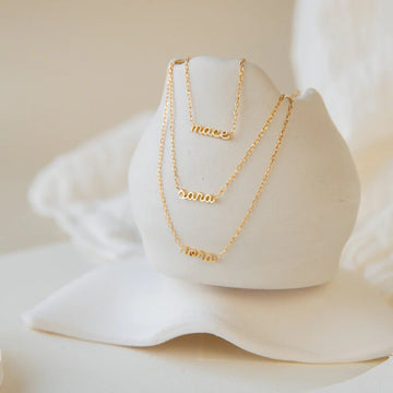 Two gold necklaces with engraved names on a white stand.