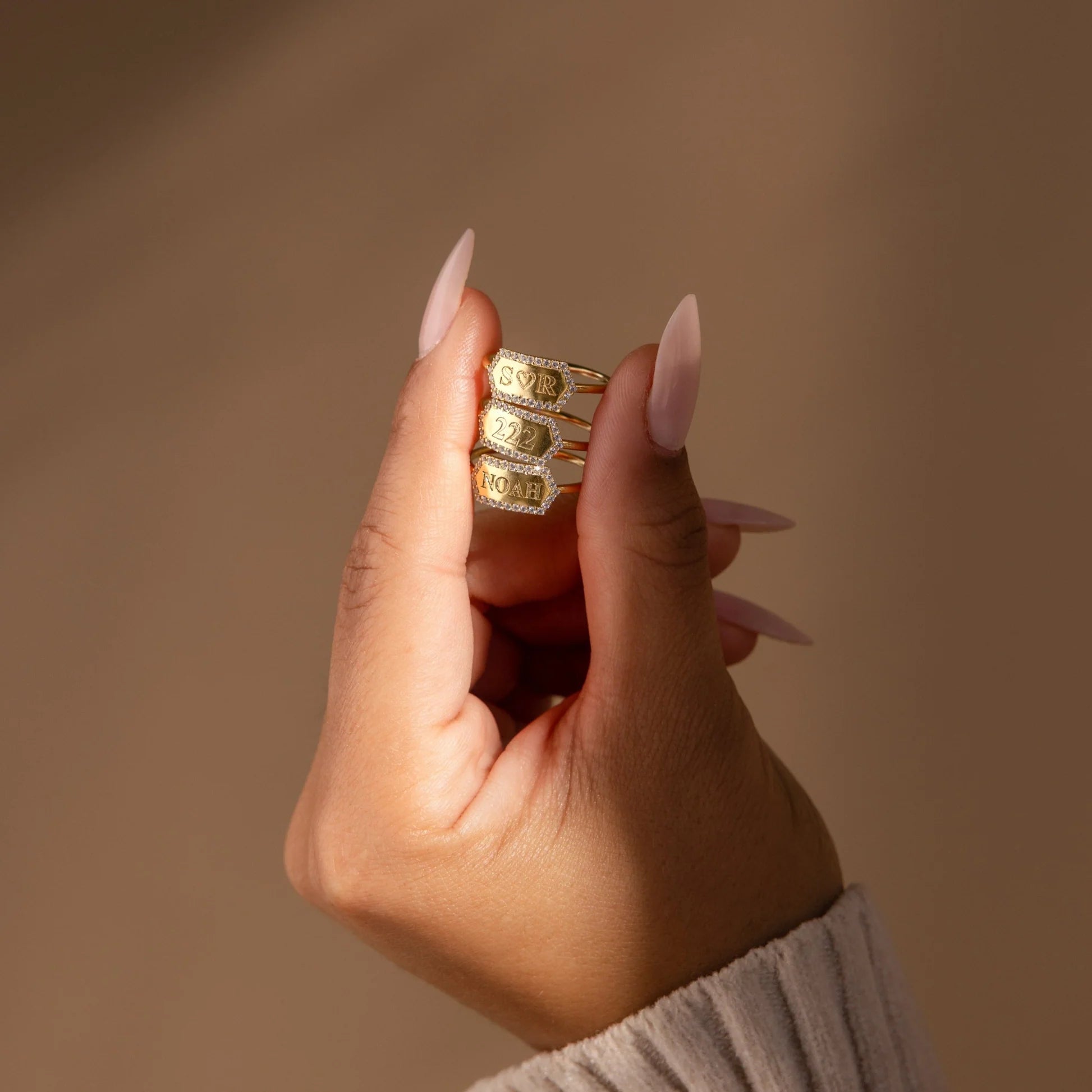 Hand wearing multiple gold rings with a neutral background