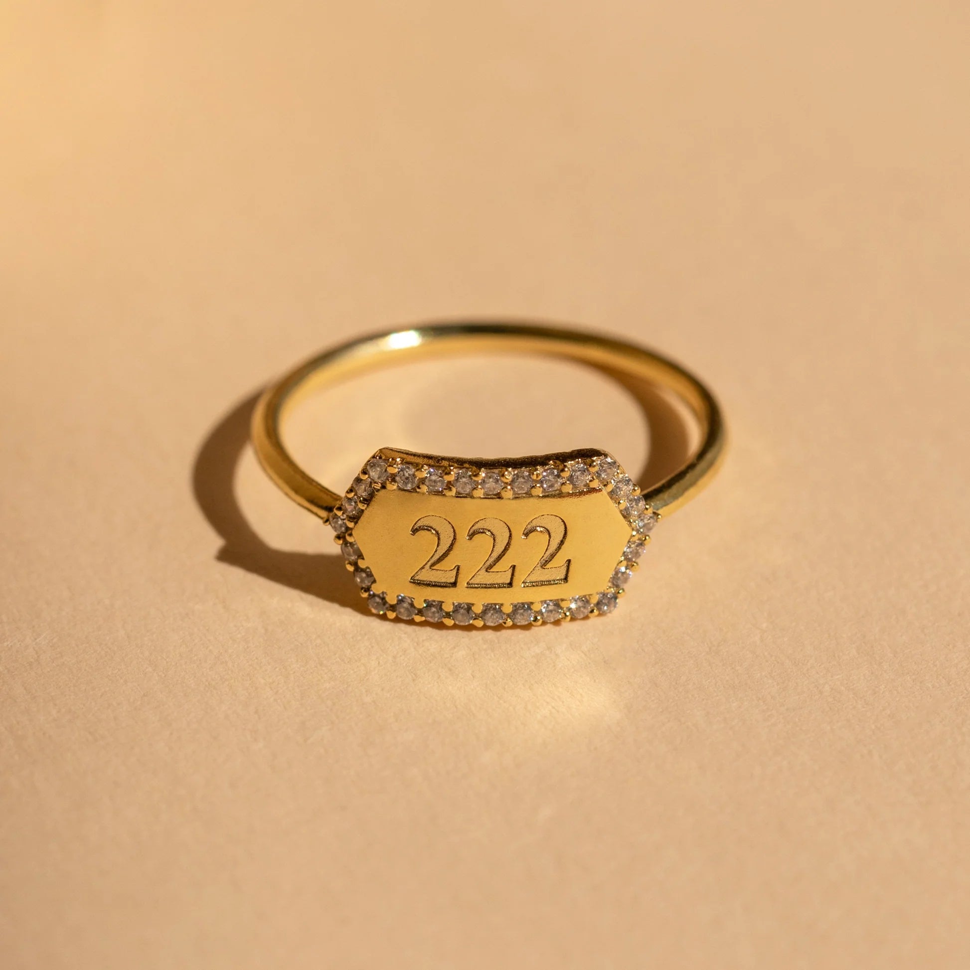 Gold ring with '222' engraving on a beige background